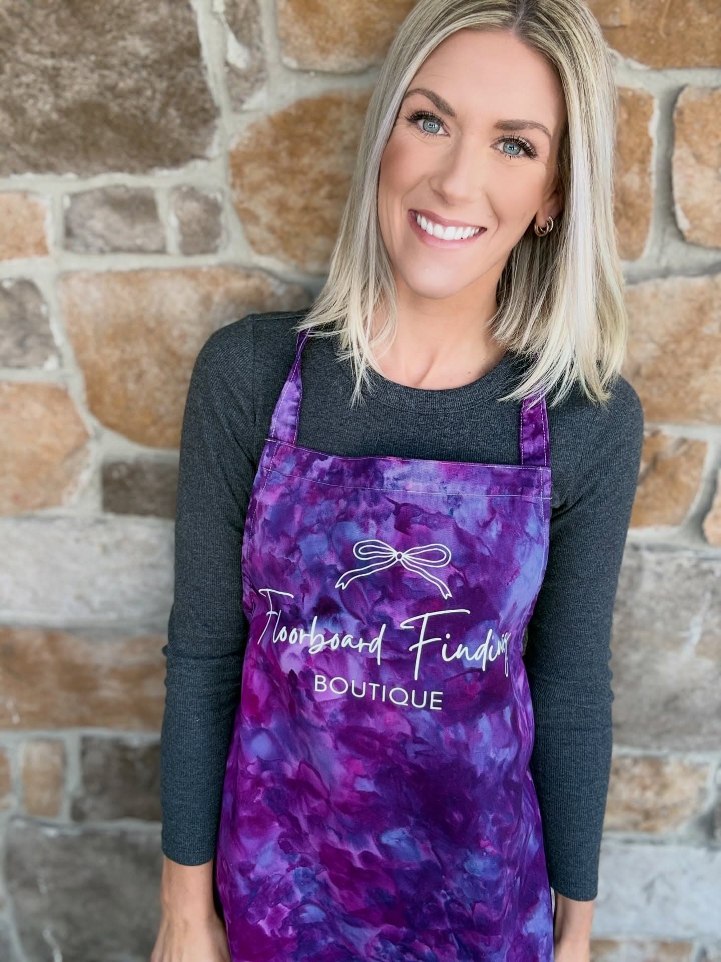 Maria smiling in her Floorboard Findings apron in front of the studio stone wall