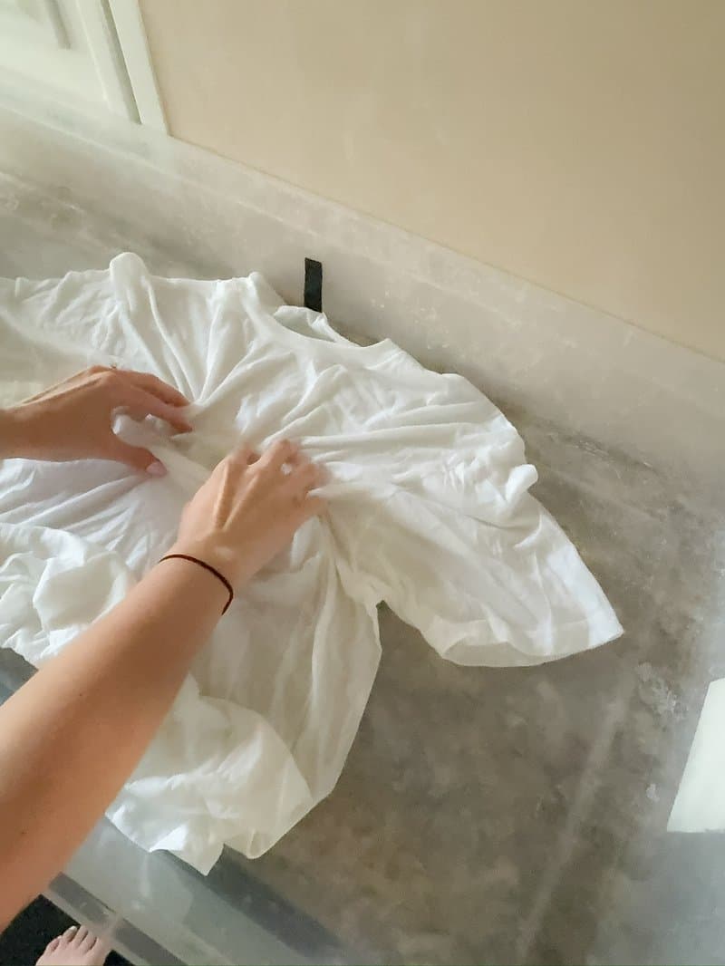Hands laying out a white blank tee on marble counter before dyeing