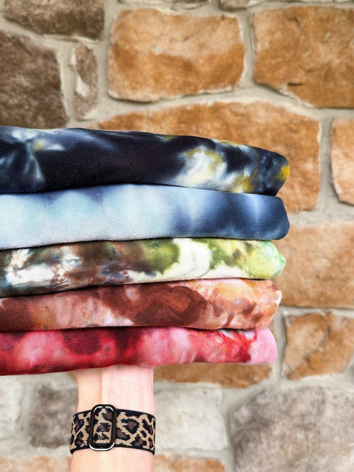 Hand holding stack of ice dyed garments against stone wall